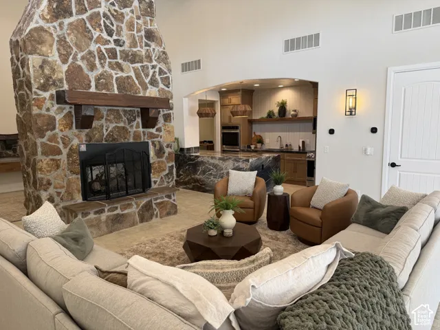 Floor-to-ceiling natural stone fireplace with a thick wood mantel, vaulted ceilings, and a kitchen featuring a large slab-stone waterfall island and built-in cabinetry