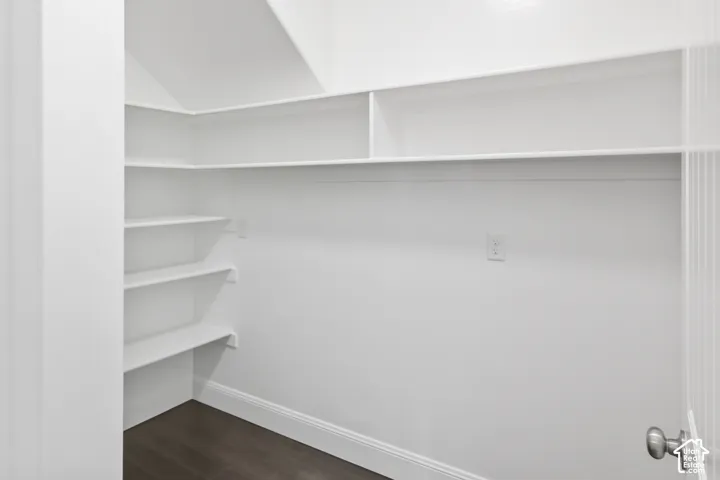 Extra-large walk-in  pantry storage area featuring white built-in shelving, dark wood-finish flooring, and electrical outlets