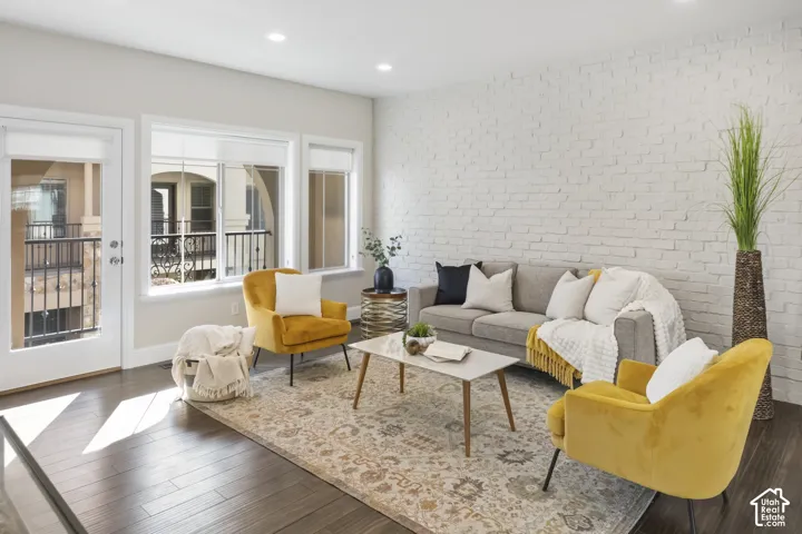 Painted brick accent wall, wood-finish flooring, recessed lighting, and multiple windows with an exterior door leading to a railed balcony