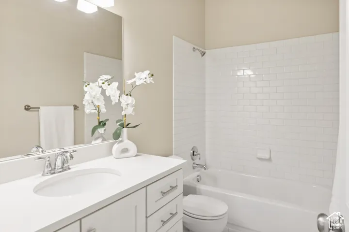 Full bathroom featuring a white vanity cabinet with a solid surface countertop, undermount sink, chrome fixtures, and a tub-shower combination with white subway tile surround