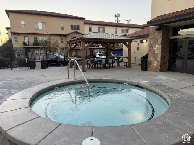 In-ground circular spa featuring concrete coping and a stainless steel handrail, accompanied by a covered timber-frame gazebo with a metal roof