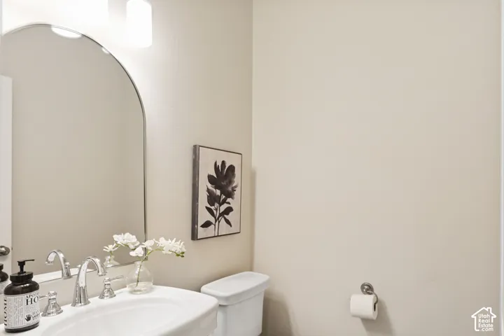 Half Bathroom on Living Level with arched wall mirror, wall-mounted light fixture, pedestal sink and natural stone slate flooring
