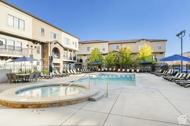 Outdoor swimming pool and stone-accented hot tub with concrete pool deck and metal perimeter fencing