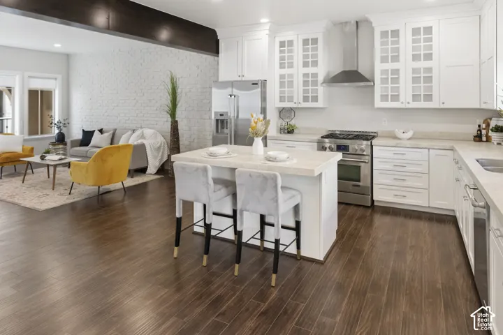 Gourmet kitchen featuring white cabinetry with paneled upper doors, high-end gas stainless steel appliances, a center island with countertop seating, wood-finish flooring, and a painted exposed brick wall
