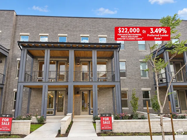 Contemporary brick exterior featuring a covered entryway, second-story balcony with metal railings, natural wood-finish soffits, and limestone-colored masonry retaining walls