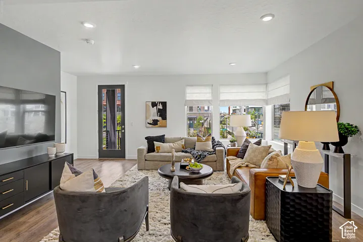 Living area featuring wood-finish flooring, recessed lighting, neutral wall palette, and expansive windows with custom Roman shades