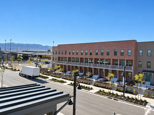 Multi-level brick exterior featuring metal-railing balconies, uniform fenestration, paved street-level entryways, and professional landscaping