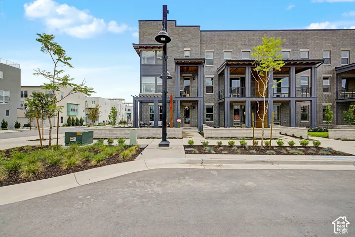 Multi-story townhome exterior featuring dark brick masonry, tiered covered balconies with metal railings, and a ground-level concrete patio with low-profile perimeter walls