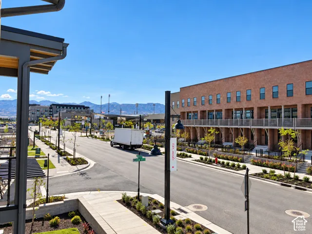 Multi-level exterior featuring red brick masonry, metal balcony railings, mountain backdrop, and professionally landscaped street-level grounds