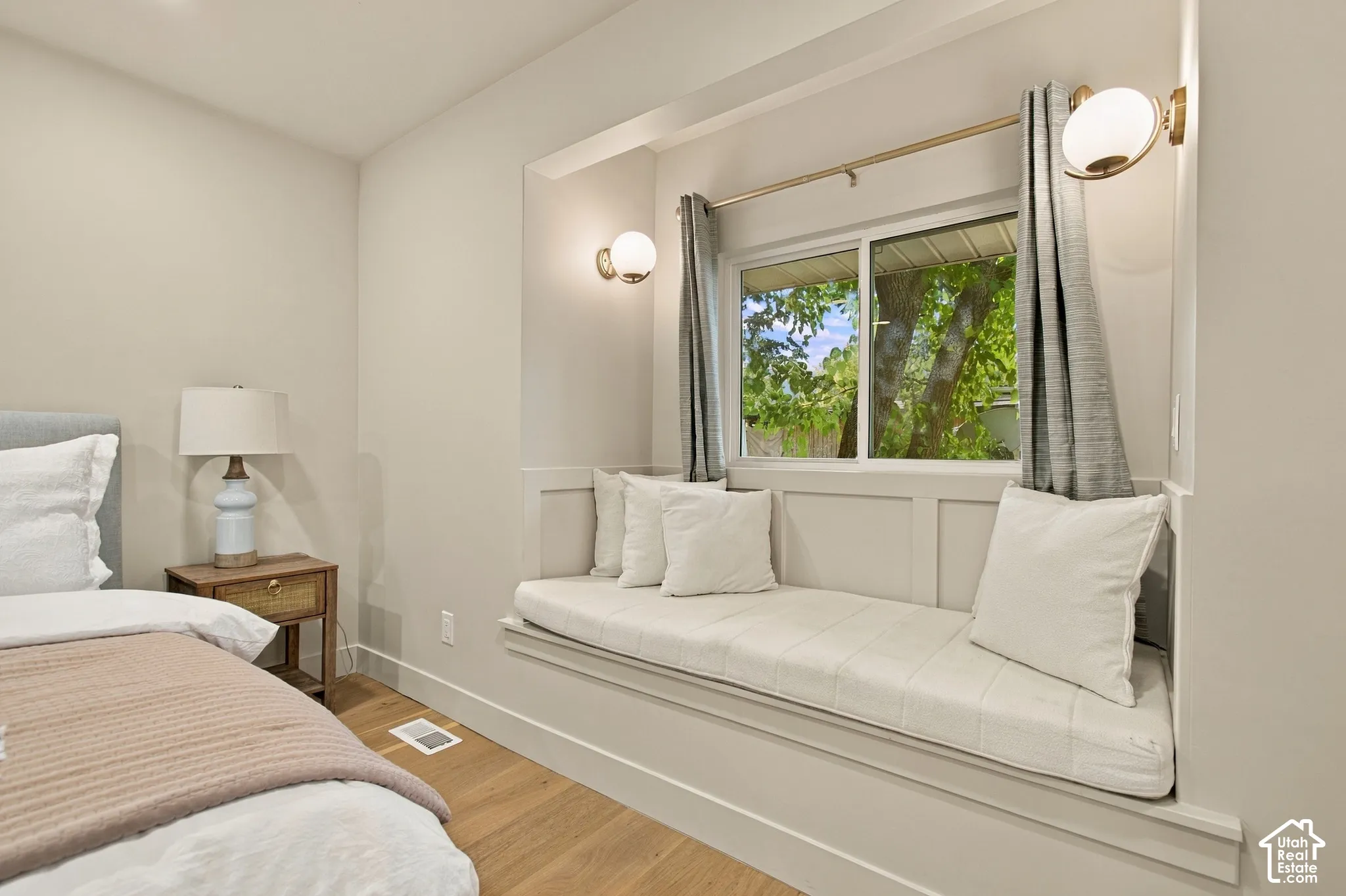 Built-in window bench seat featuring millwork detailing, dual wall-mounted globe sconces, and wood-finish flooring