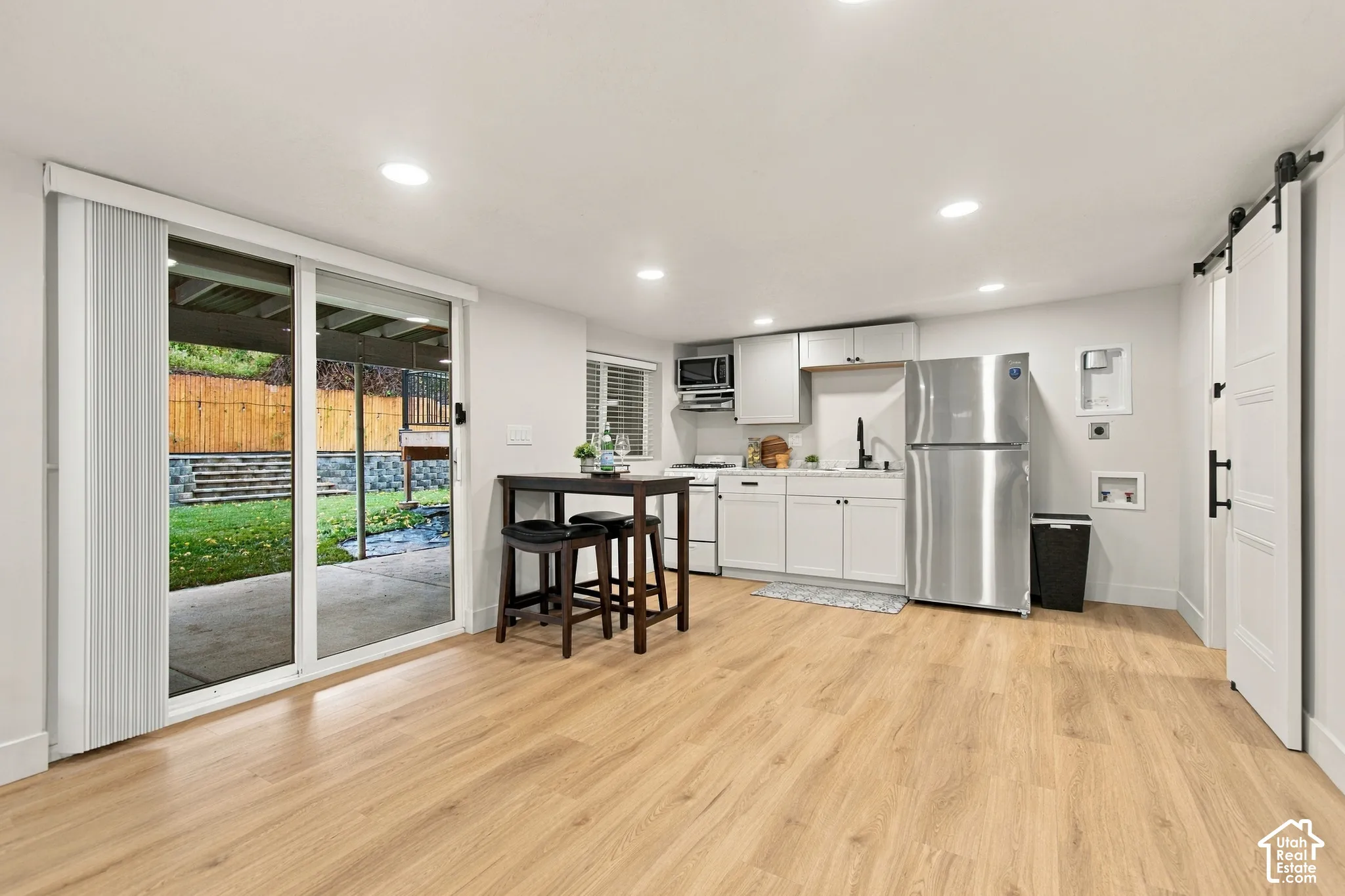 Wood-finish flooring, sliding glass door, white shaker-style cabinetry, stainless steel refrigerator, and interior sliding barn door
