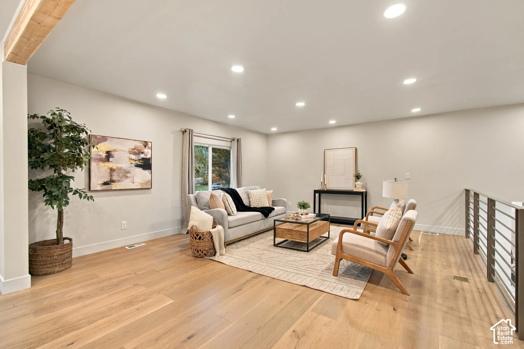 Open-concept interior featuring light wood-finish flooring, recessed lighting, exposed ceiling beam, and metal horizontal-bar railing
