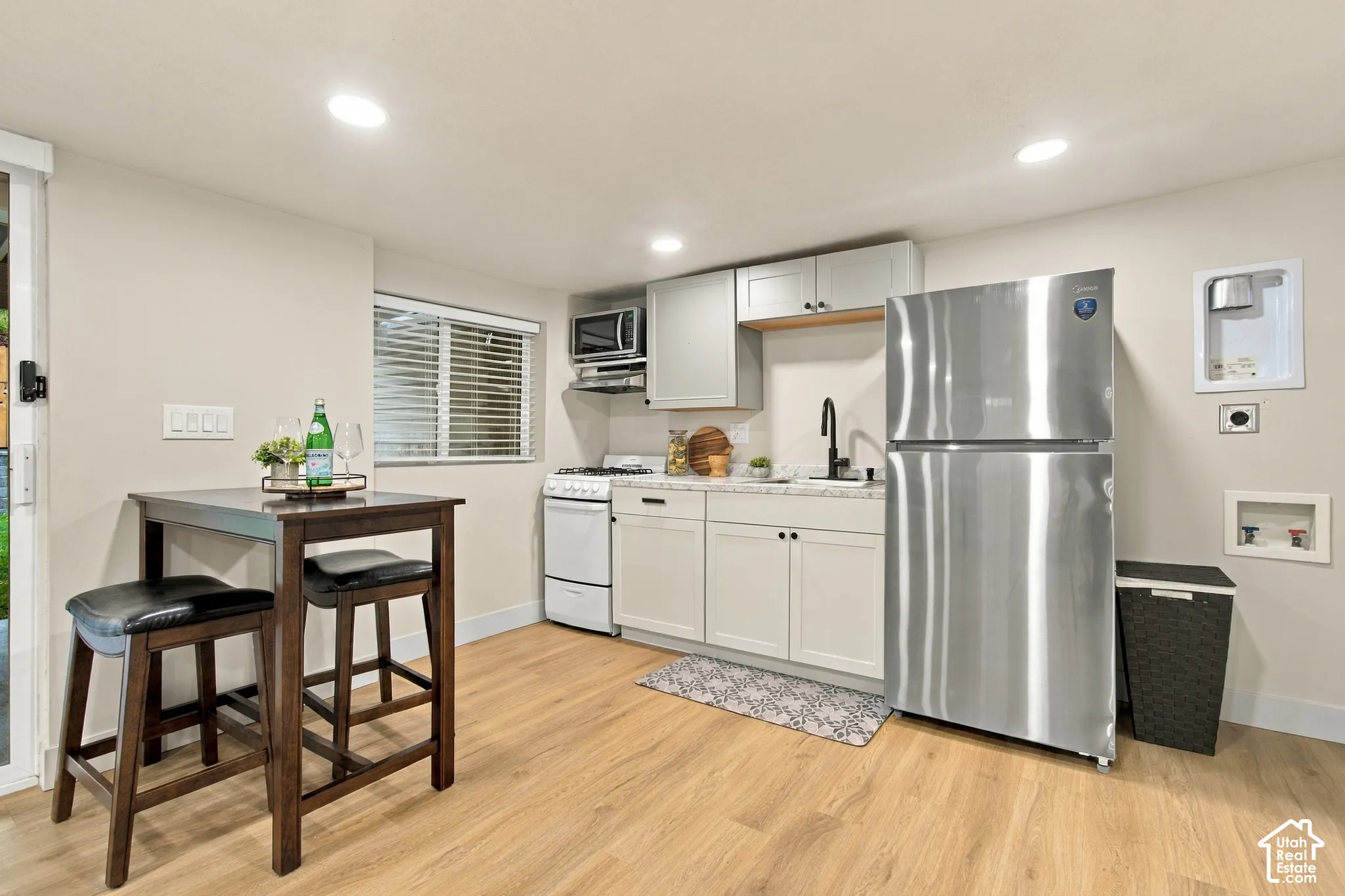 Kitchenette featuring Shaker-style cabinetry, a stainless steel refrigerator, a compact gas range, a sink with a matte black faucet, and wood-finish flooring