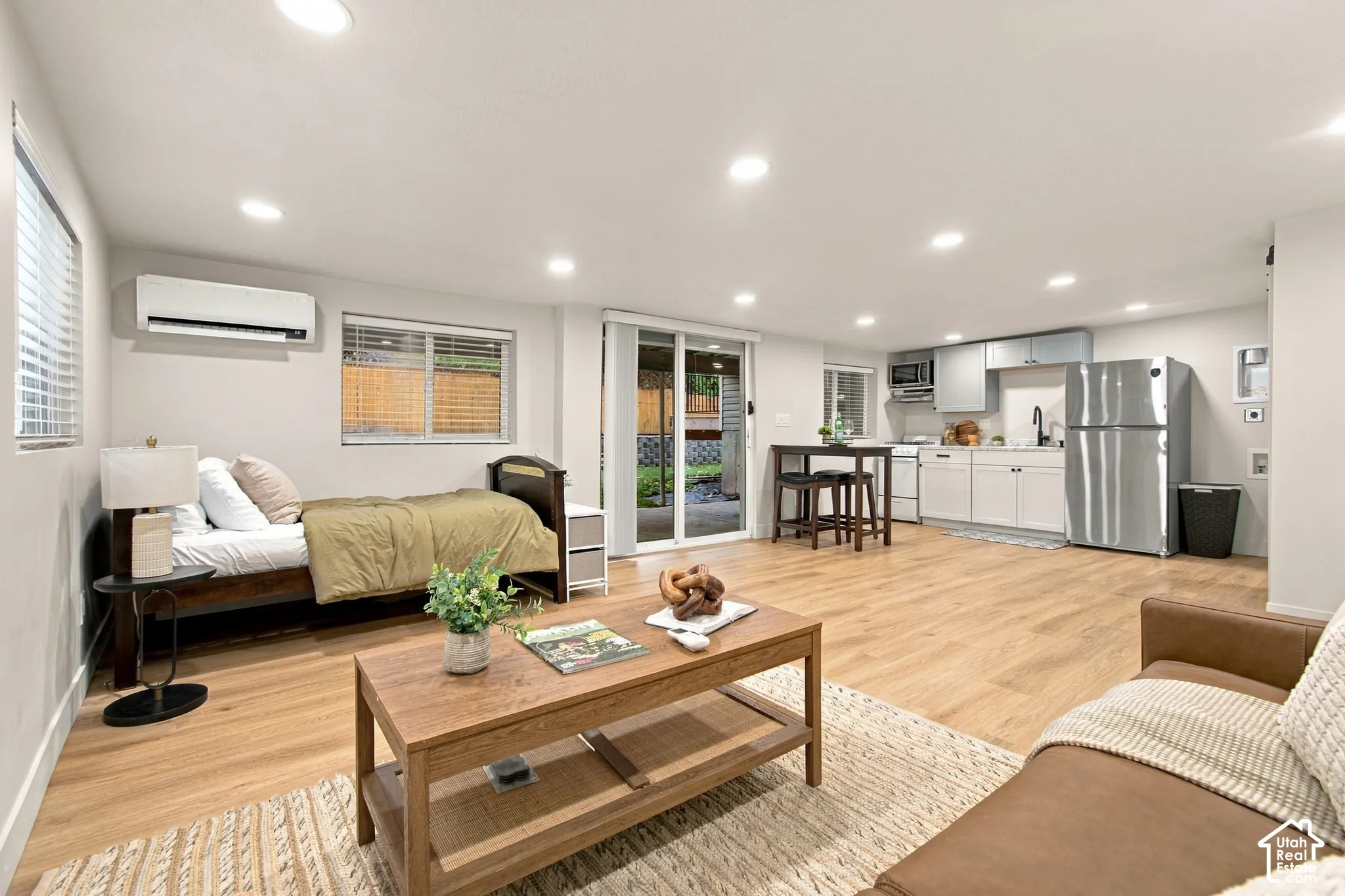 Open-concept space featuring wood-finish flooring, recessed lighting, a kitchenette with stainless steel appliances, and a wall-mounted ductless heating and cooling unit