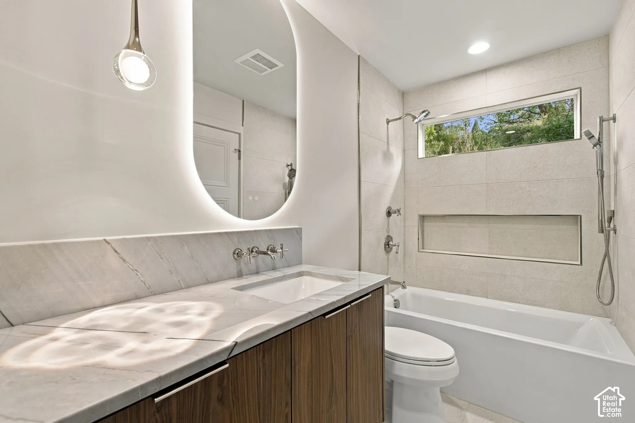 Modern vanity featuring wood-finish cabinetry, stone countertop, integrated vessel sink, and backlit oval mirror
