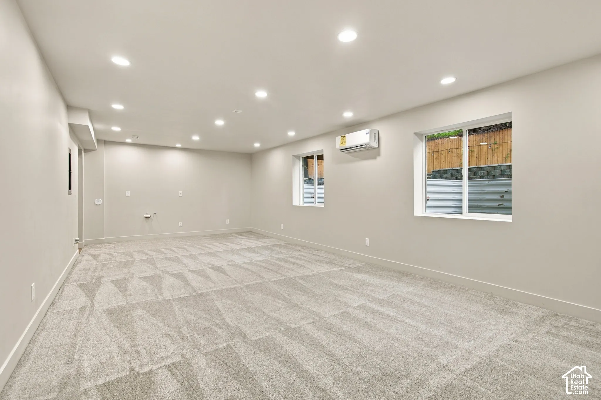 Neutral interior featuring wall-to-wall carpeting, recessed ceiling lighting, dual windows, and a wall-mounted ductless climate control unit