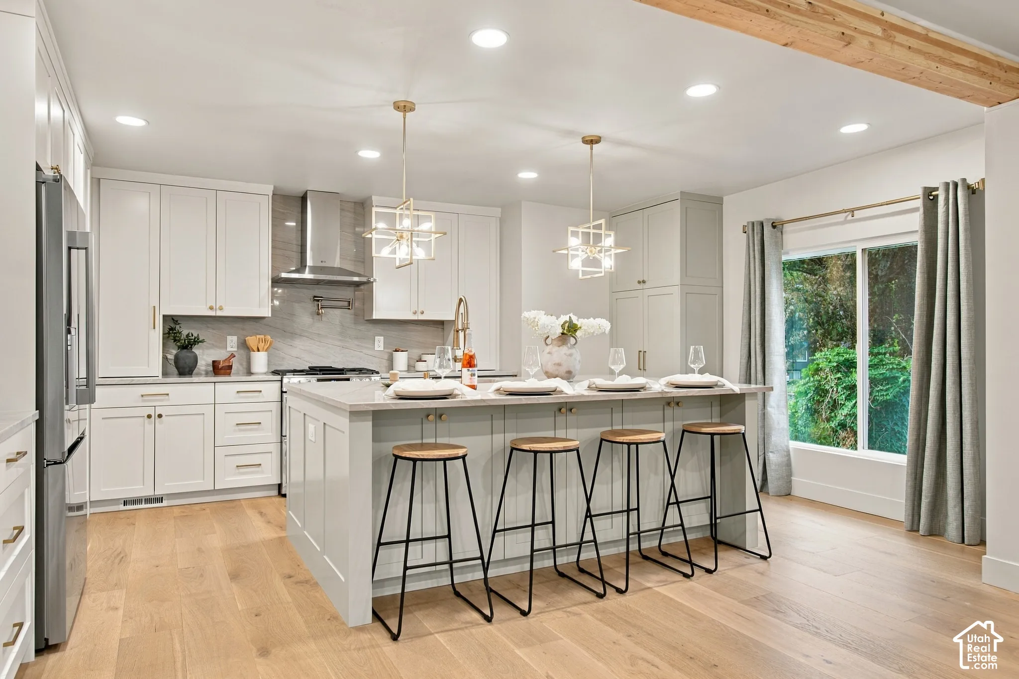 Kitchen featuring white shaker-style cabinetry, a central island with countertop seating, stone-finish backsplash, stainless steel range hood, and wood-finish flooring