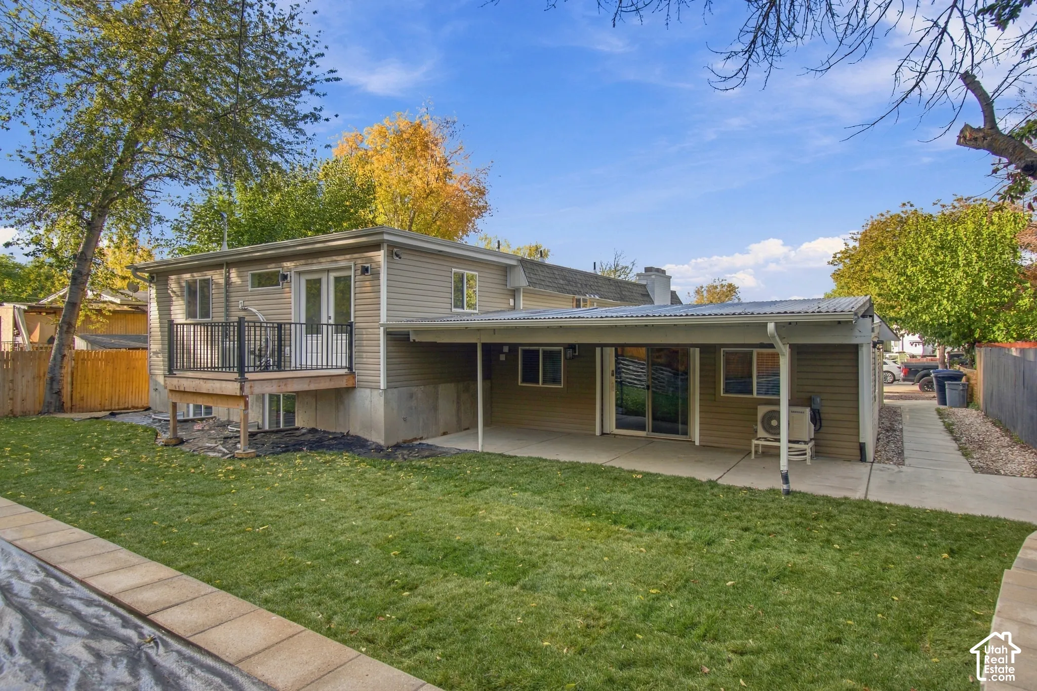 Backyard featuring a raised wooden deck with metal railings, a covered concrete patio, siding exterior, and a manicured lawn