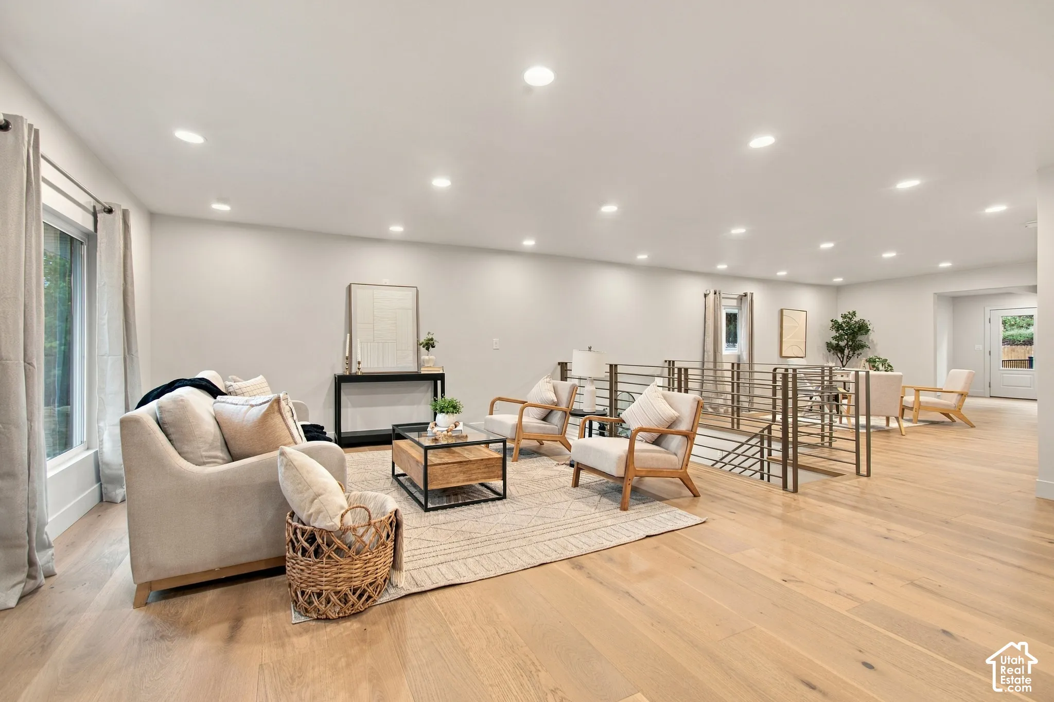 Open-concept living space featuring wood-finish flooring, recessed lighting, and a metal horizontal-bar stair railing