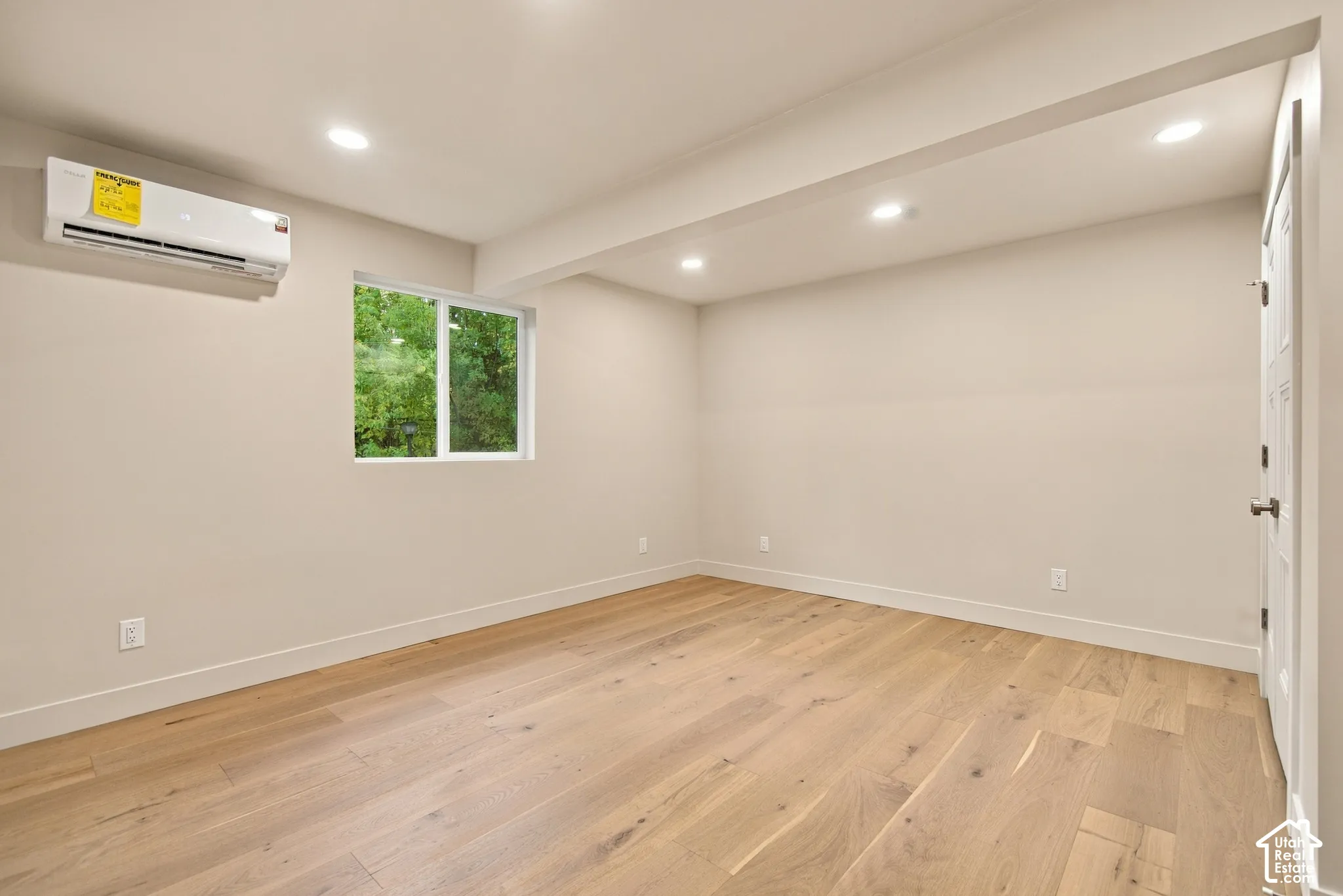 Interior space featuring wood-finish flooring, recessed lighting, a wall-mounted ductless climate control unit, and a single-pane window