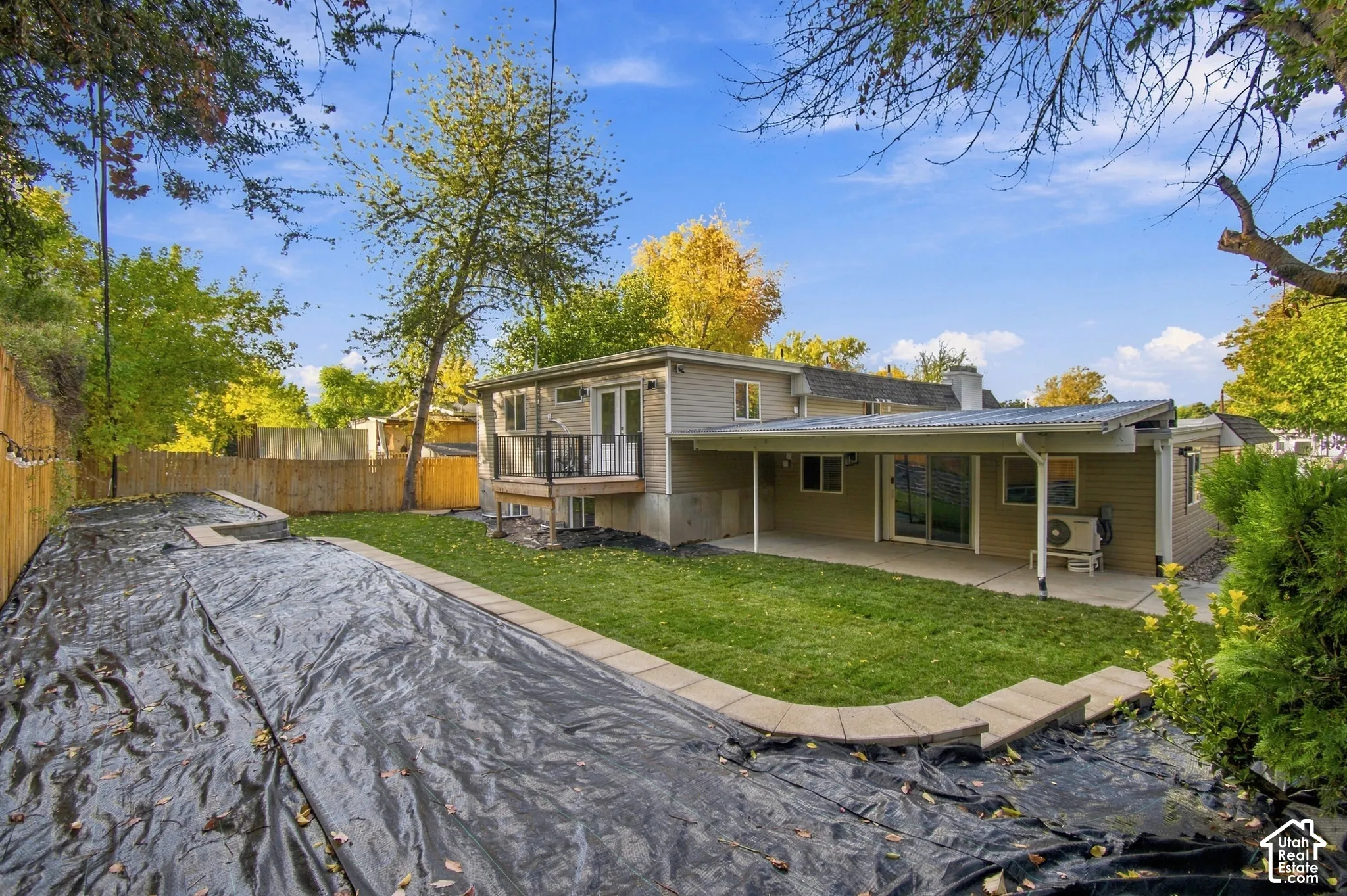 Exterior featuring a raised deck with metal railing, a covered concrete patio, tiered retaining walls, and a wood privacy fence