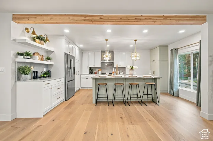 Kitchen featuring white shaker-style cabinetry, central island with seating, exposed wood ceiling beam, wood-finish flooring, and open shelving