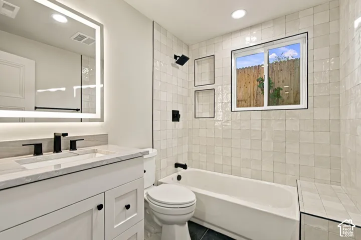 White vanity cabinet with stone-finish countertop, integrated under-mount sink, matte black faucet, wall-mounted LED-backlit mirror, and tile shower surround with dual built-in recessed niches