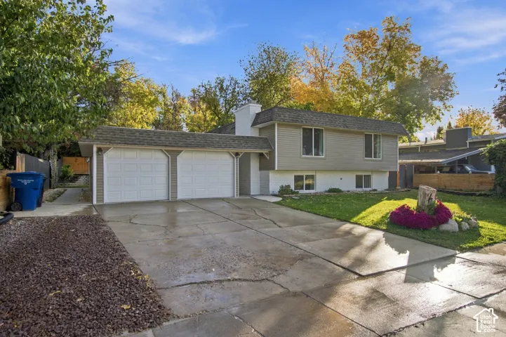 Split-level exterior featuring horizontal siding, a concrete driveway, an attached two-car garage, and landscaped front lawn with stone-bordered flower beds