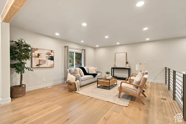Open-concept interior featuring light wood-finish flooring, recessed lighting, exposed ceiling beam, and metal horizontal-bar railing