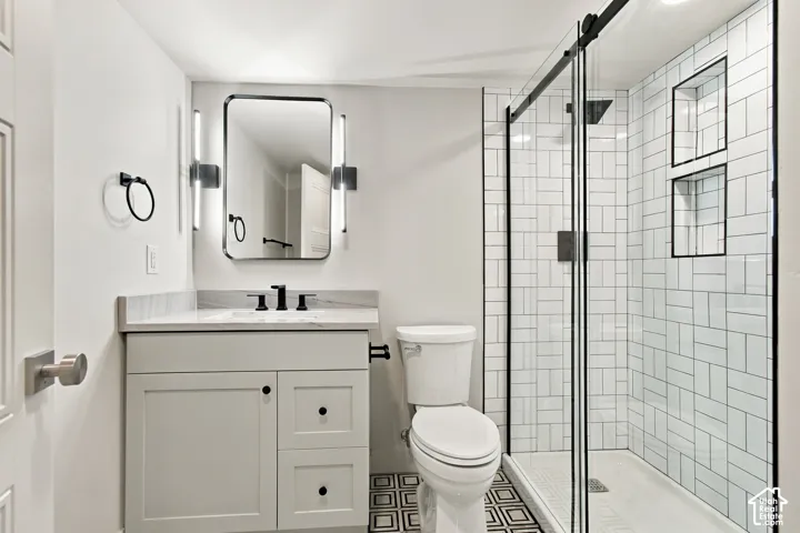 Bathroom featuring a vanity with white cabinetry, stone-finish countertop, and matte black fixtures, paired with a glass-enclosed shower with white subway tile surround and integrated dual shelving niches