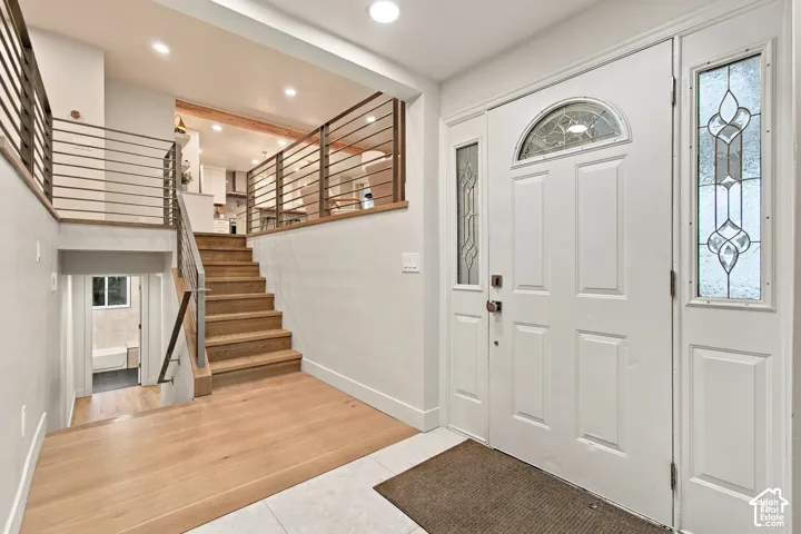 Foyer featuring an entry door with decorative glass sidelights, wood-finish flooring, recessed lighting, and horizontal cable railing along the staircase