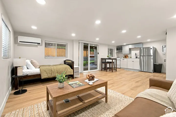 Open-concept space featuring wood-finish flooring, recessed lighting, a kitchenette with stainless steel appliances, and a wall-mounted ductless heating and cooling unit