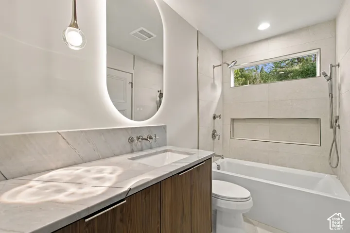 Modern vanity featuring wood-finish cabinetry, stone countertop, integrated vessel sink, and backlit oval mirror