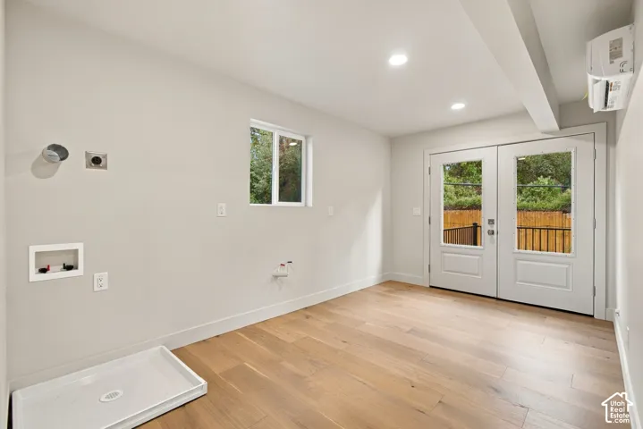 Utility area featuring wood-finish flooring, recessed lighting, wall-mounted climate control unit, single-hung window, and glass-paneled double doors