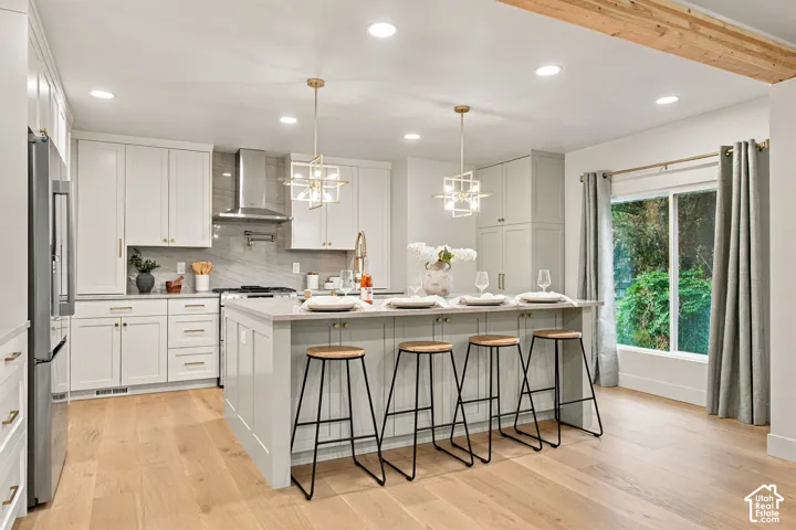 Kitchen featuring white shaker-style cabinetry, a central island with countertop seating, stone-finish backsplash, stainless steel range hood, and wood-finish flooring