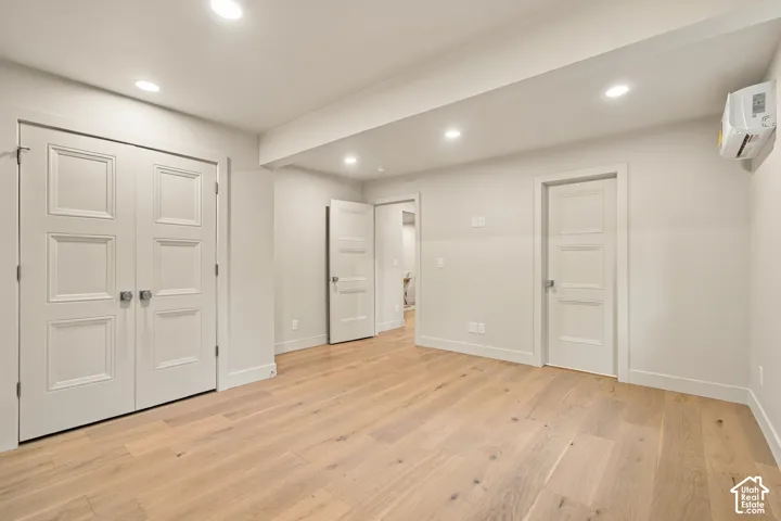 Room featuring wood-finish flooring, recessed lighting, wall-mounted climate control unit, and three-panel interior doors