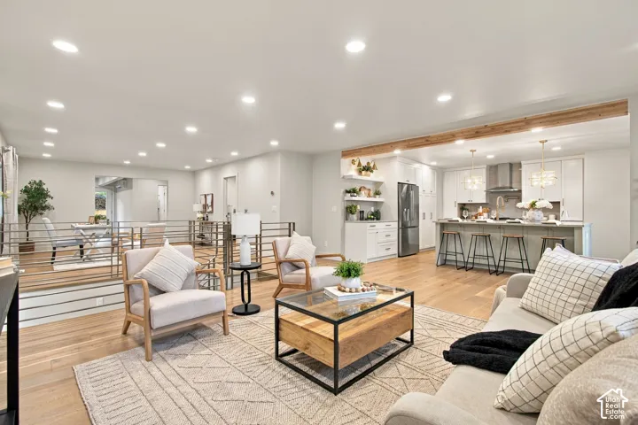 Open-concept living space featuring wood-finish flooring, recessed lighting, exposed ceiling beam, kitchen island with seating, and horizontal metal stair railing