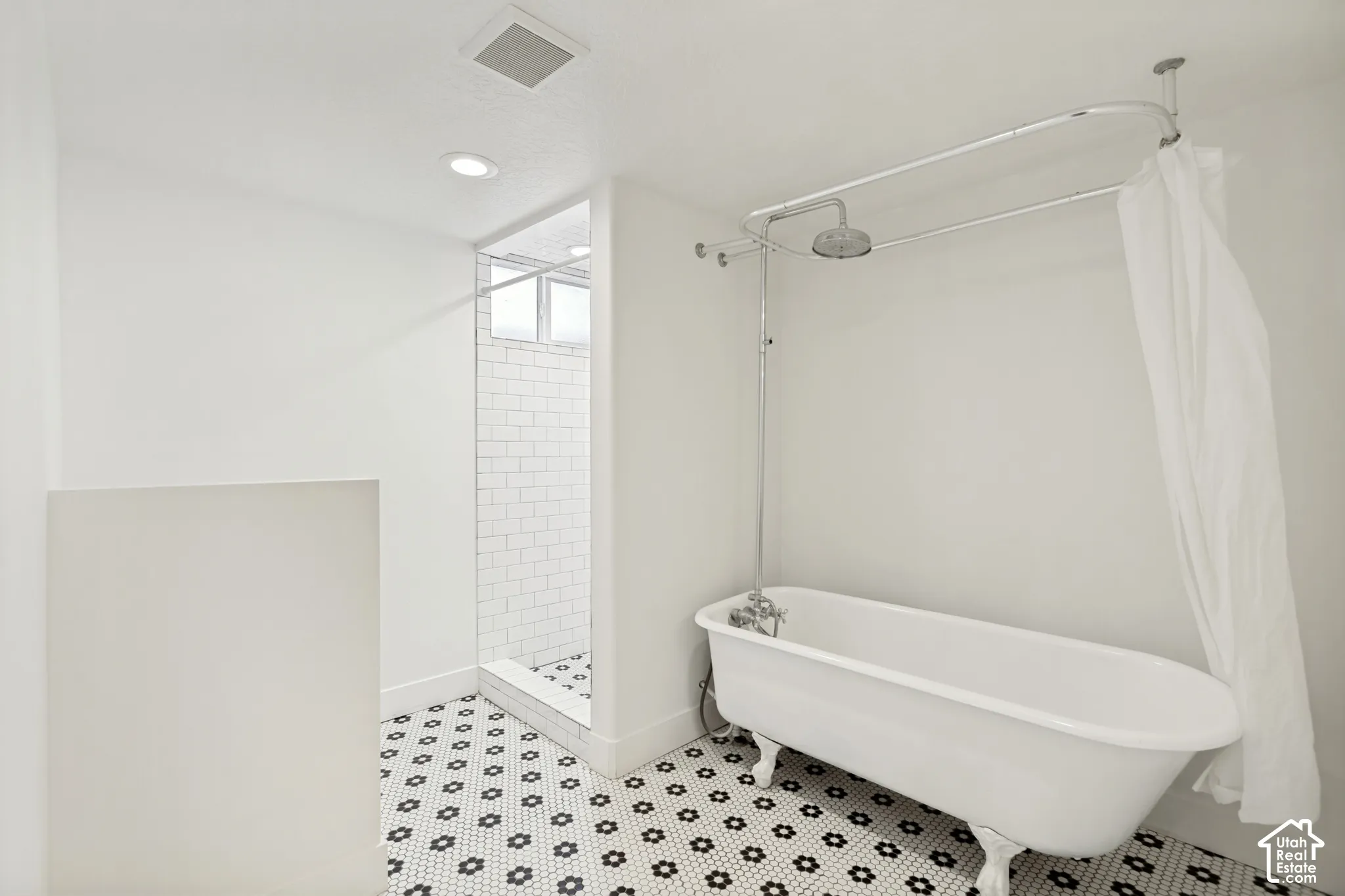 Clawfoot soaking tub with a chrome shower assembly, walk-in shower with white subway tile surround, and geometric patterned floor tile