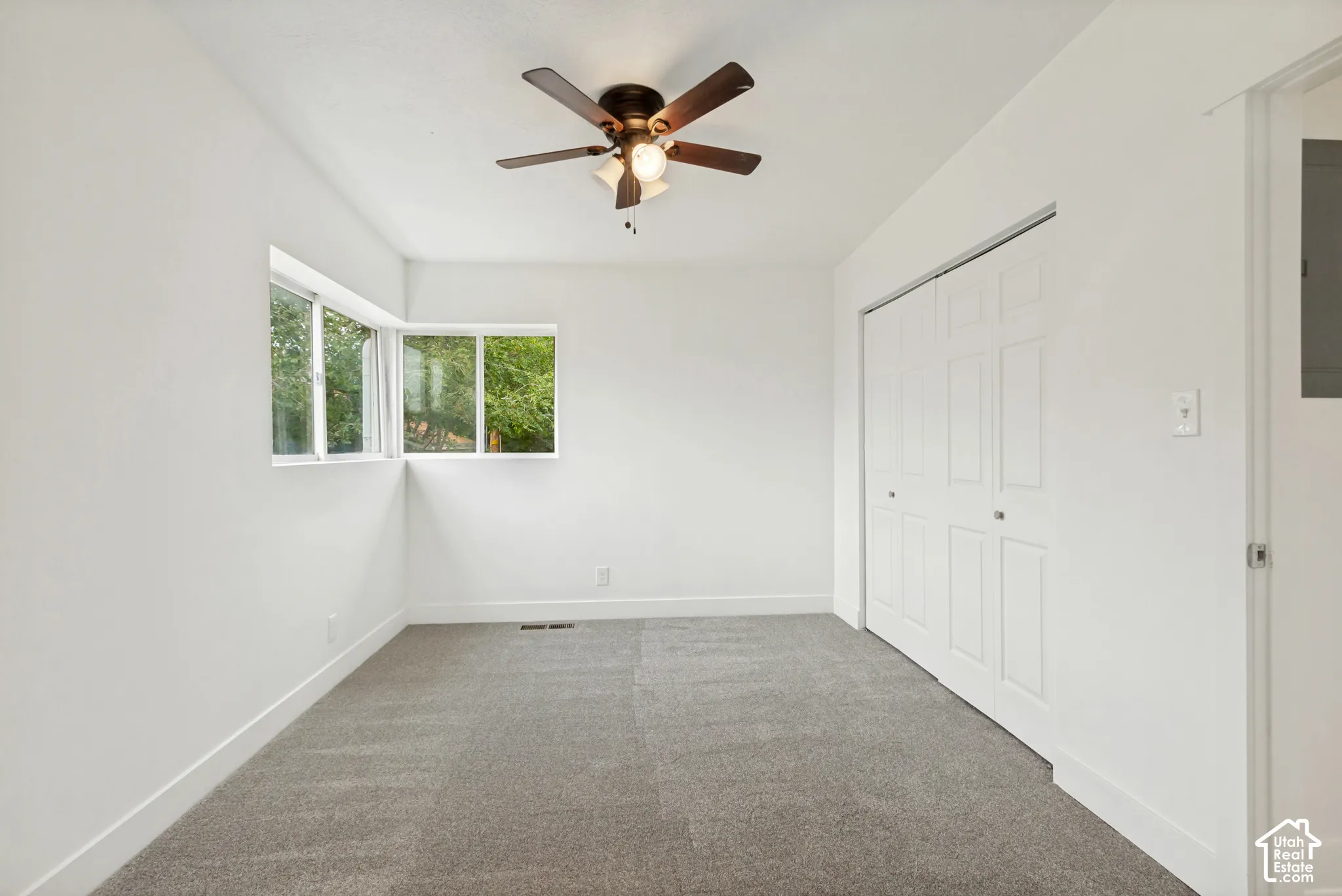 Neutral-toned carpeting, corner windows, built-in closet with multi-panel doors, and a ceiling fan with integrated lighting