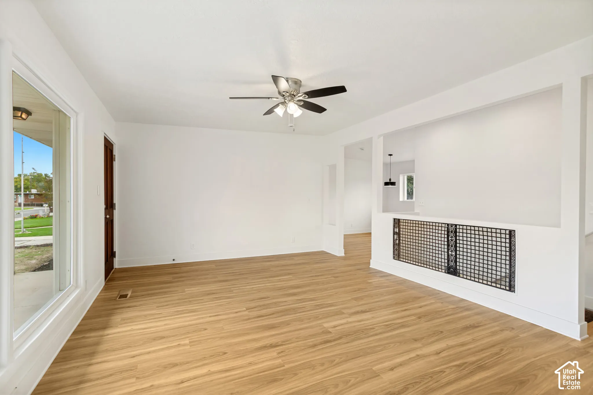 Living area featuring wood-finish flooring, a ceiling fan with integrated lighting, a large picture window, and a decorative interior metal lattice screen