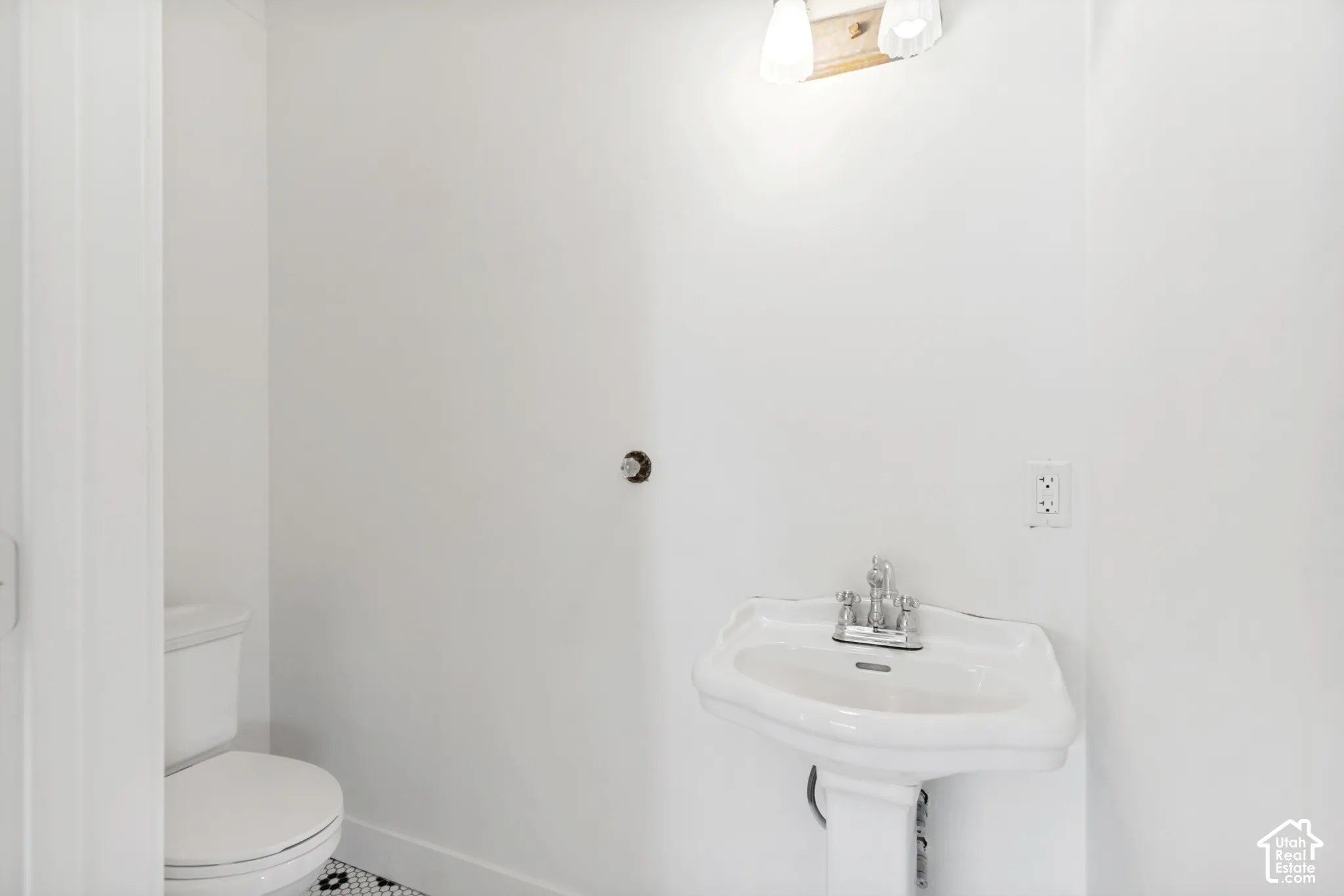 Pedestal sink with polished chrome faucet, white porcelain toilet, and geometric patterned floor tiling