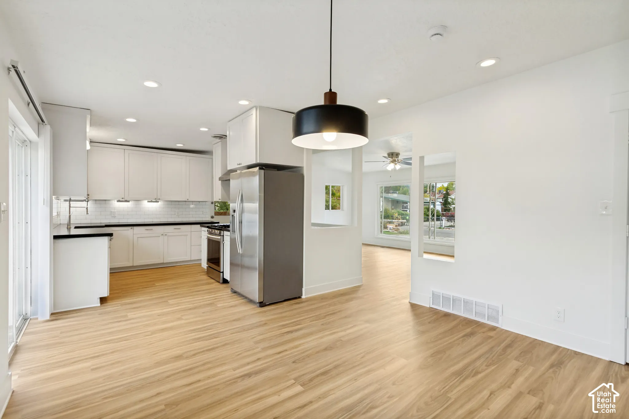 Kitchen featuring white cabinetry, subway tile backsplash, wood-finish flooring, stainless steel appliances, and a minimalist pendant light