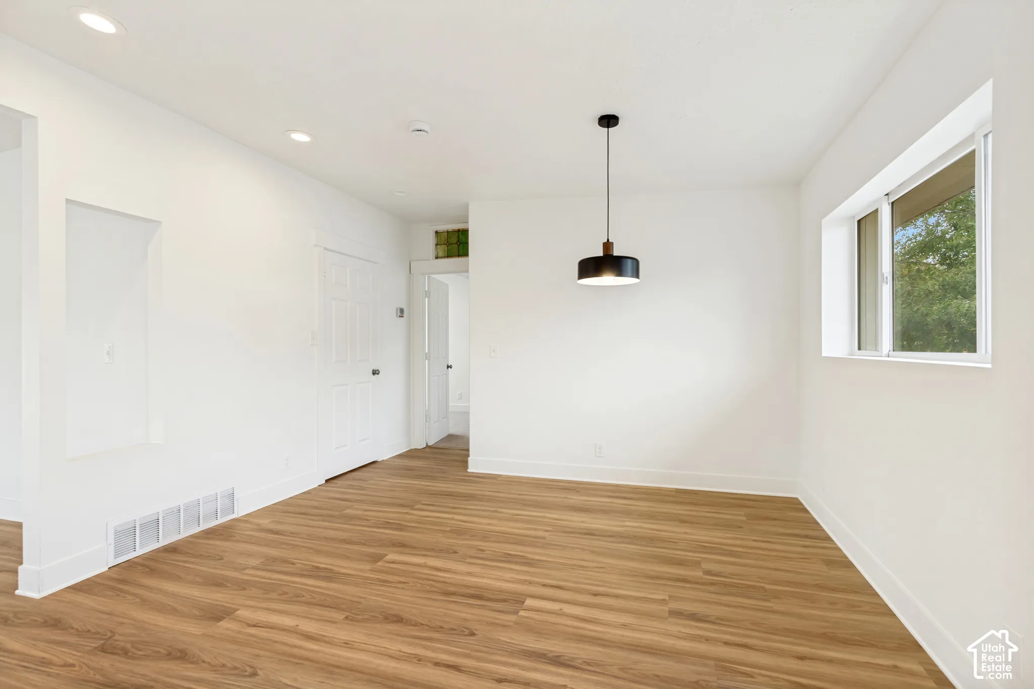 Neutral interior featuring wood-finish flooring, recessed lighting, a minimalist pendant light, and a recessed wall niche