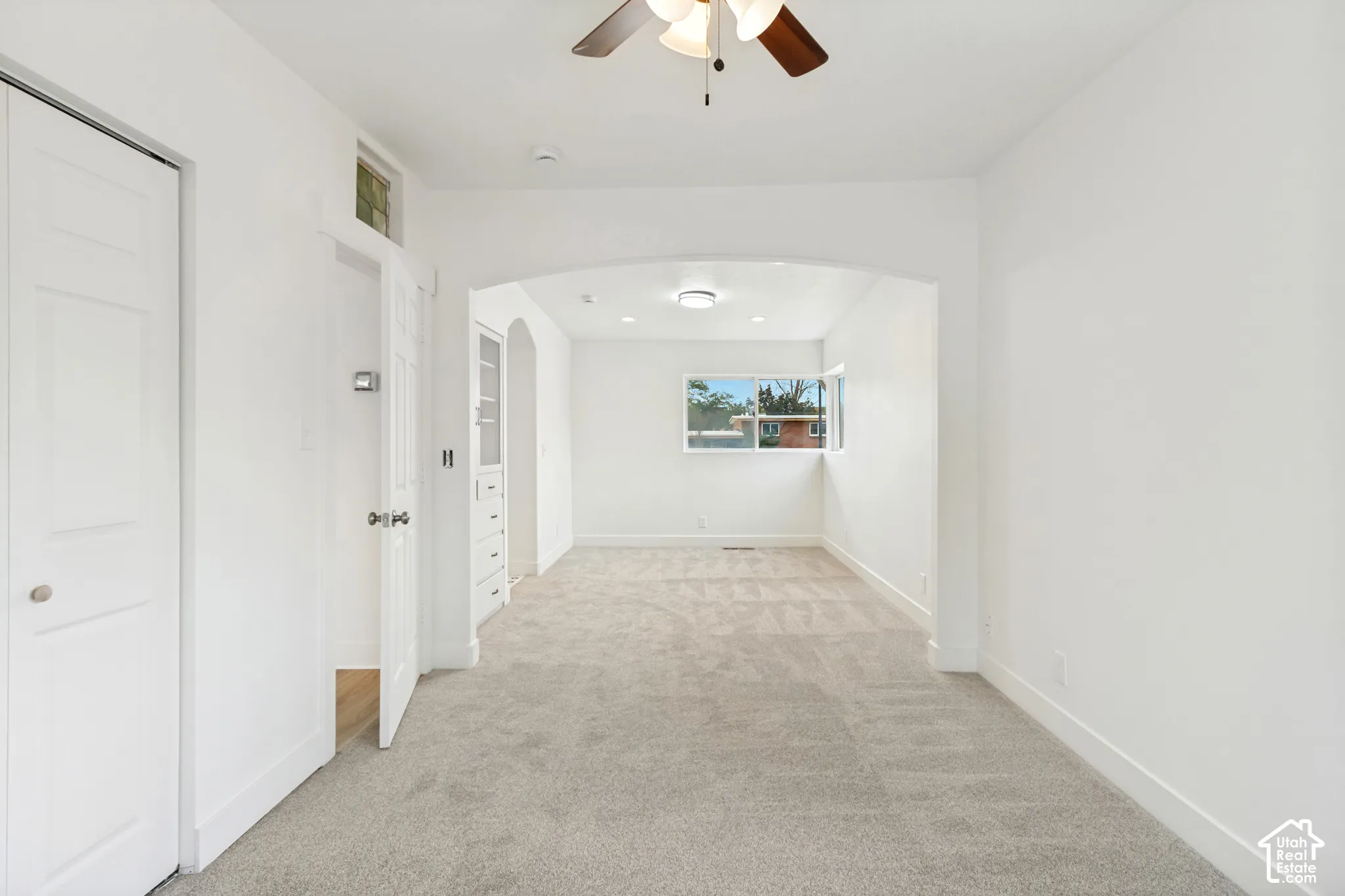 Room featuring neutral carpeting, an arched architectural detail, built-in cabinetry, ceiling fan with light fixture, and horizontal window