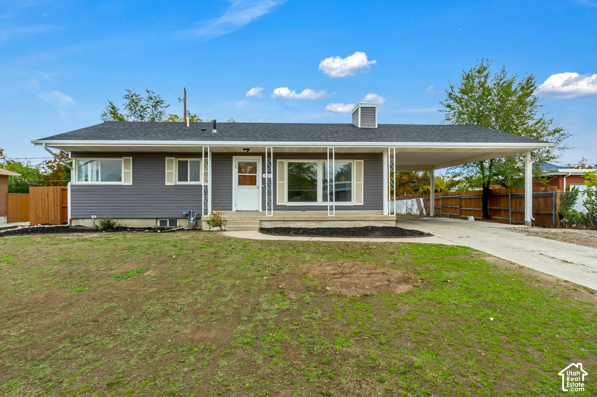 Single-story residence featuring grey horizontal siding, a covered carport, shutter-framed windows, and a concrete front porch