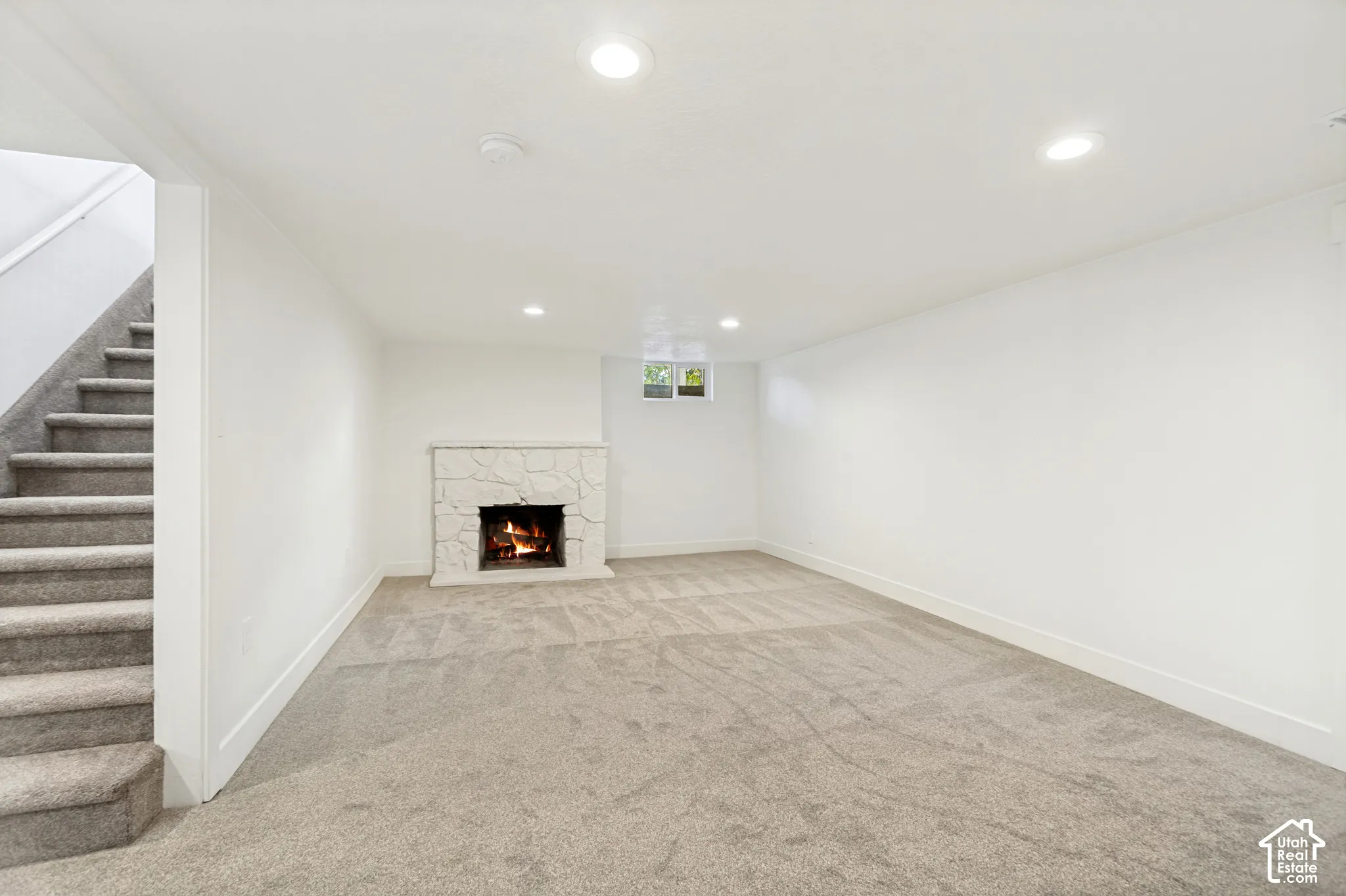Finished room featuring a stone-clad fireplace, neutral wall-to-wall carpeting, recessed ceiling lighting, and a staircase with carpeted treads