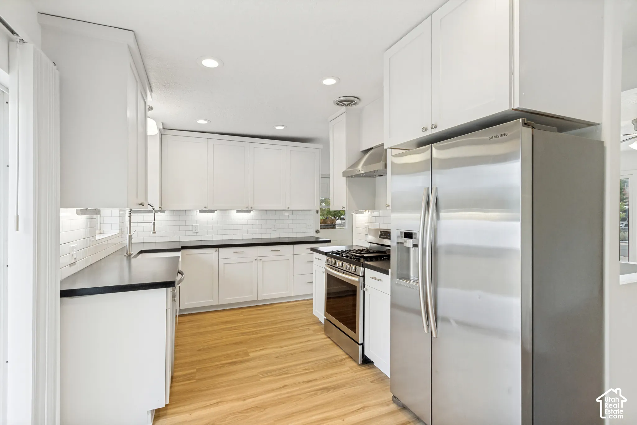 Kitchen featuring white cabinetry, solid-surface countertops, white subway tile backsplash, stainless steel appliances, and wood-finish flooring