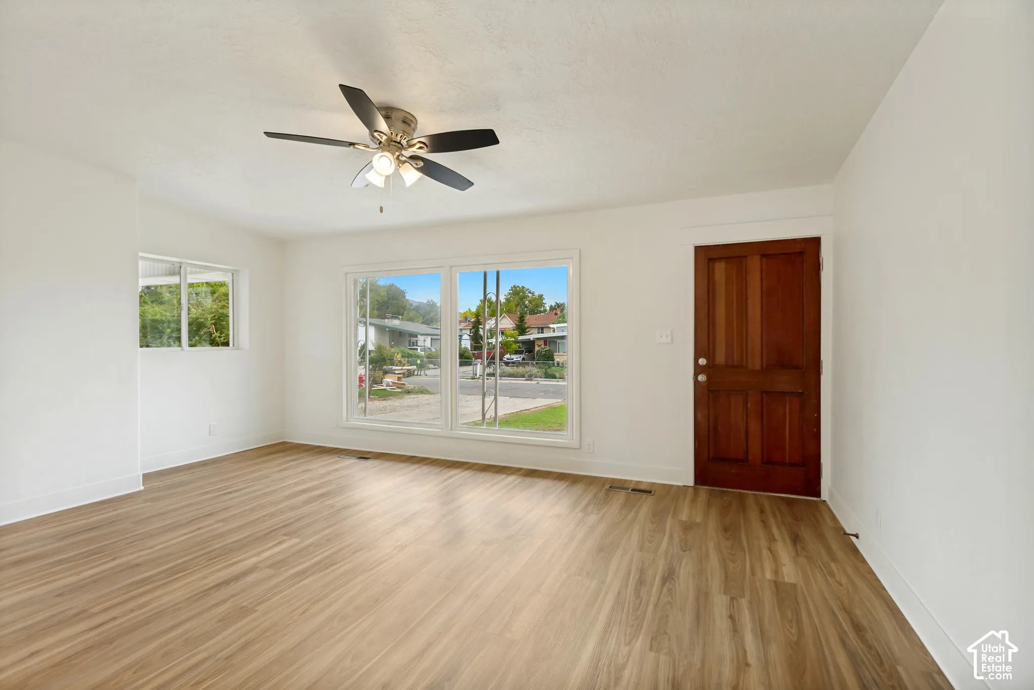 Neutral interior space featuring wood-finish flooring, a wood-panel entry door, large windows, and a ceiling-mounted light fixture