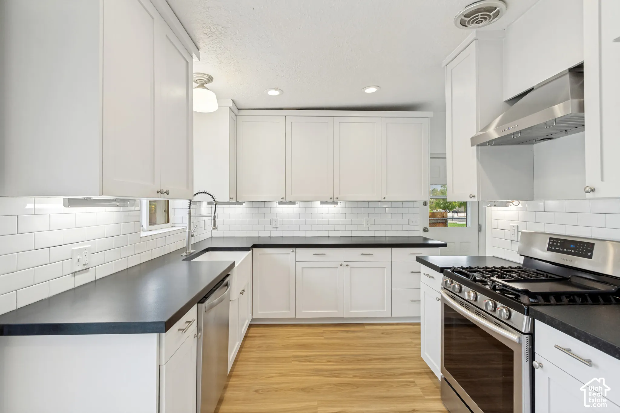 Kitchen featuring white cabinetry, dark countertops, a farmhouse-style sink, subway tile backsplash, and stainless steel appliances