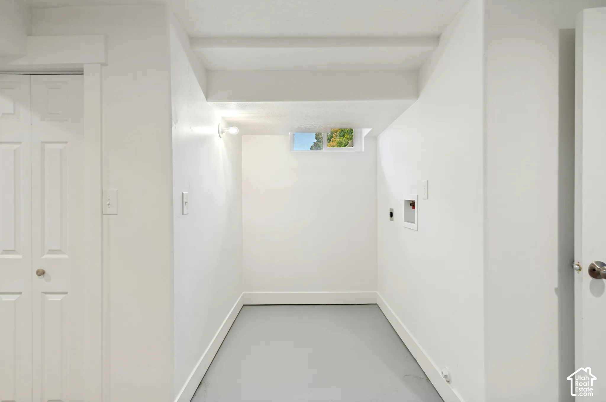 Neutral interior space featuring white walls, gray floor, bi-fold closet door, utility connections, and a rectangular window